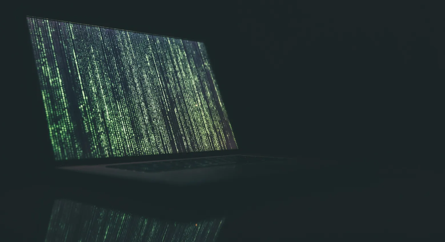 An open laptop with a bright green, futuristic pattern on screen, sitting on a reflective surface in a dark room.