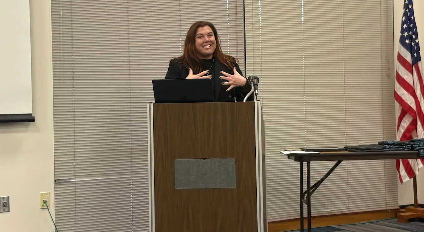 A woman giving a speech, standing behind a wooden lectern.